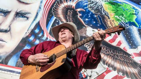 Kraig Moss, a supporter of Donald Trump during the campaign, sings a song outside a truck with a Trump painting last year in Iowa. Now, he regrets doing so.