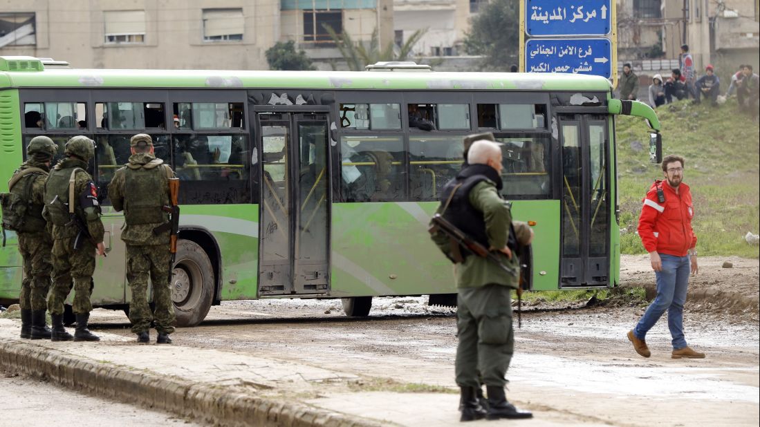 Members of the Russian military police and Syrian regime soldiers stand guard as a bus drives by. 