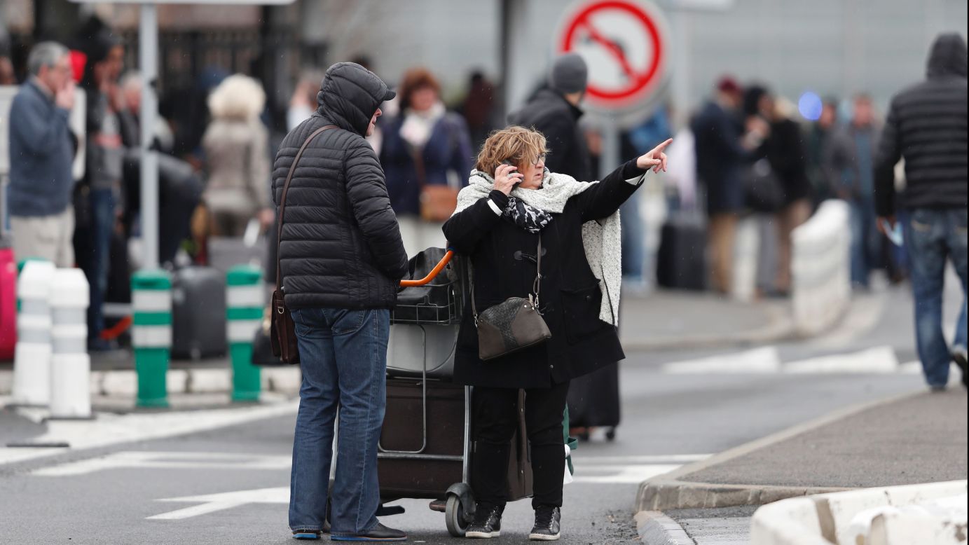A woman talks on her cell phone as travelers evacuate Paris' Orly airport.