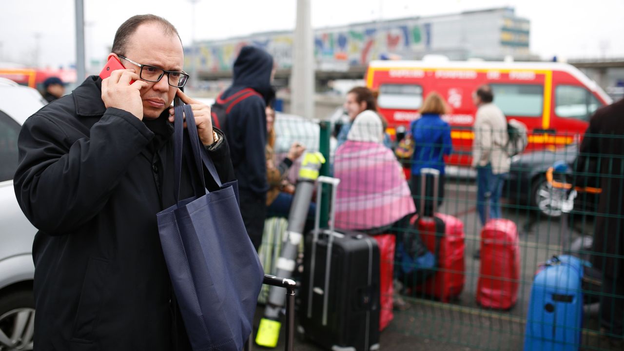 A man talks on his cell phone as travelers evacuate the airport.