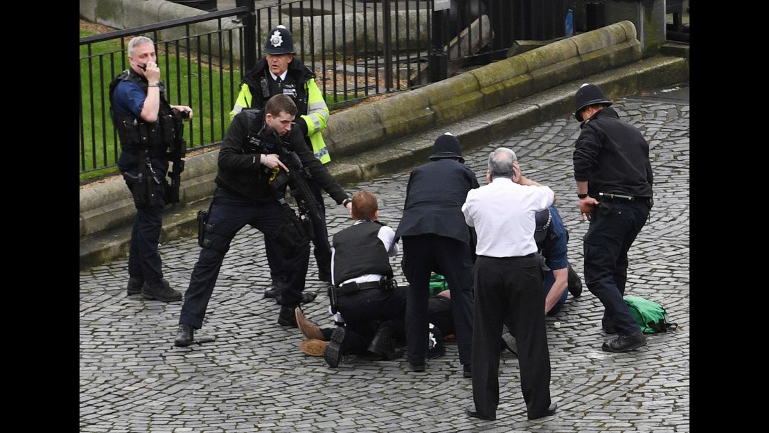 A policeman points a gun at a man on the floor as emergency services attend the scene outside the Palace of Westminster.