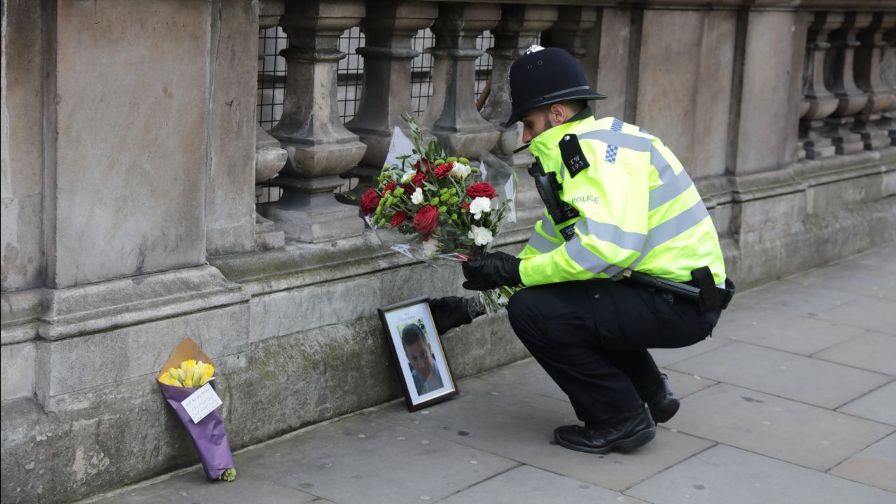 A police officer lays a floral tribute from a member of the public beside a photo of Keith Palmer, the Metropolitan Police constable who was stabbed to death near the Houses of Parliament in London during a terror attack on March 23, 2017.