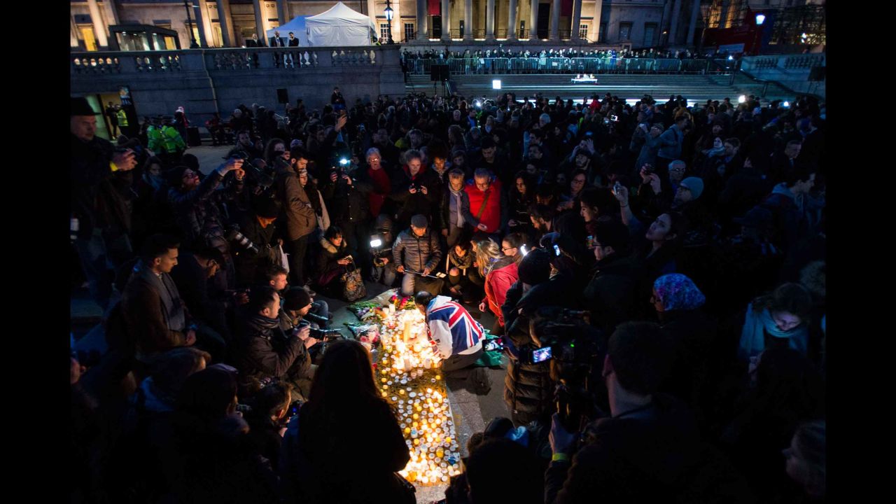 The crowd huddles around 62-year-old John Loughrey (center, draped in Union Jack flag) as he lights candles in tribute to the victims.
