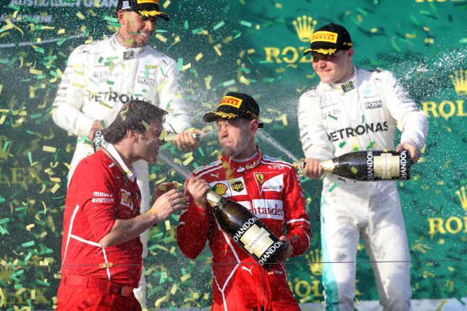 Vettel celebrates on the podium with one of the Ferrari engineers. Second-placed Lewis Hamiton and new Mercedes teammate Valtteri Bottas, who finished third, are in the background.