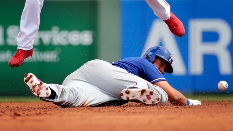 Texas Rangers' James Loney is hit by the ball while diving back to second base as Los Angeles Angels' Andrelton Simmons leaps out of the way during a spring training game, on Wednesday, March 22.
