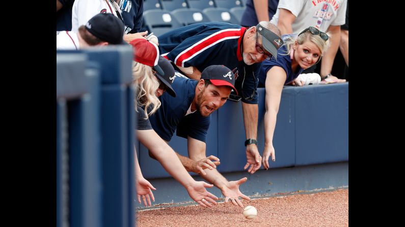 Fans reach over the wall for baseballs rolled to them by Atlanta Braves coaches before a spring training baseball game against the Washington Nationals on Tuesday, March 21, in West Palm Beach, Florida. 