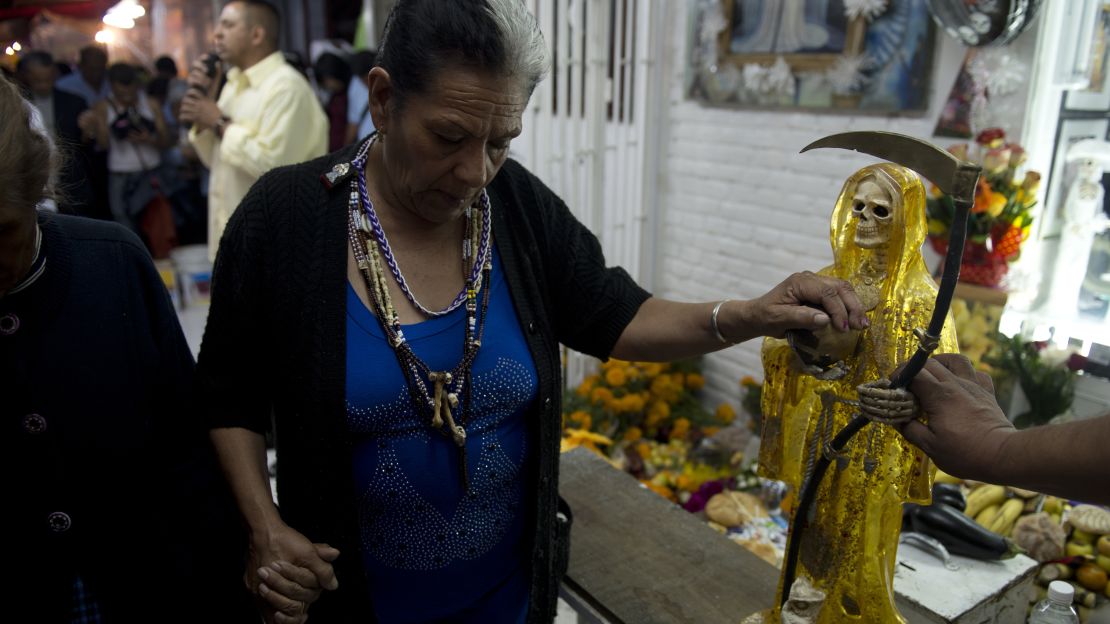 Doña Queta Romero touches a Santa Muerte statue outside her home.