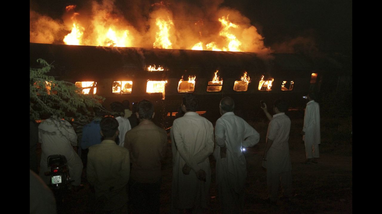 People look at a burning passenger train in Sheikhupura, Pakistan, on Tuesday, March 28. Authorities said the train collided with an oil-tanker truck, killing at least one person and injuring others.