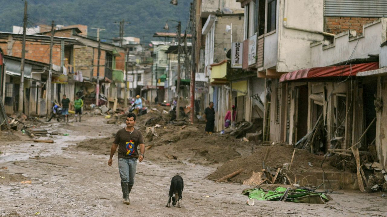 A man and a dog walk down a mud-filled street in Mocoa.