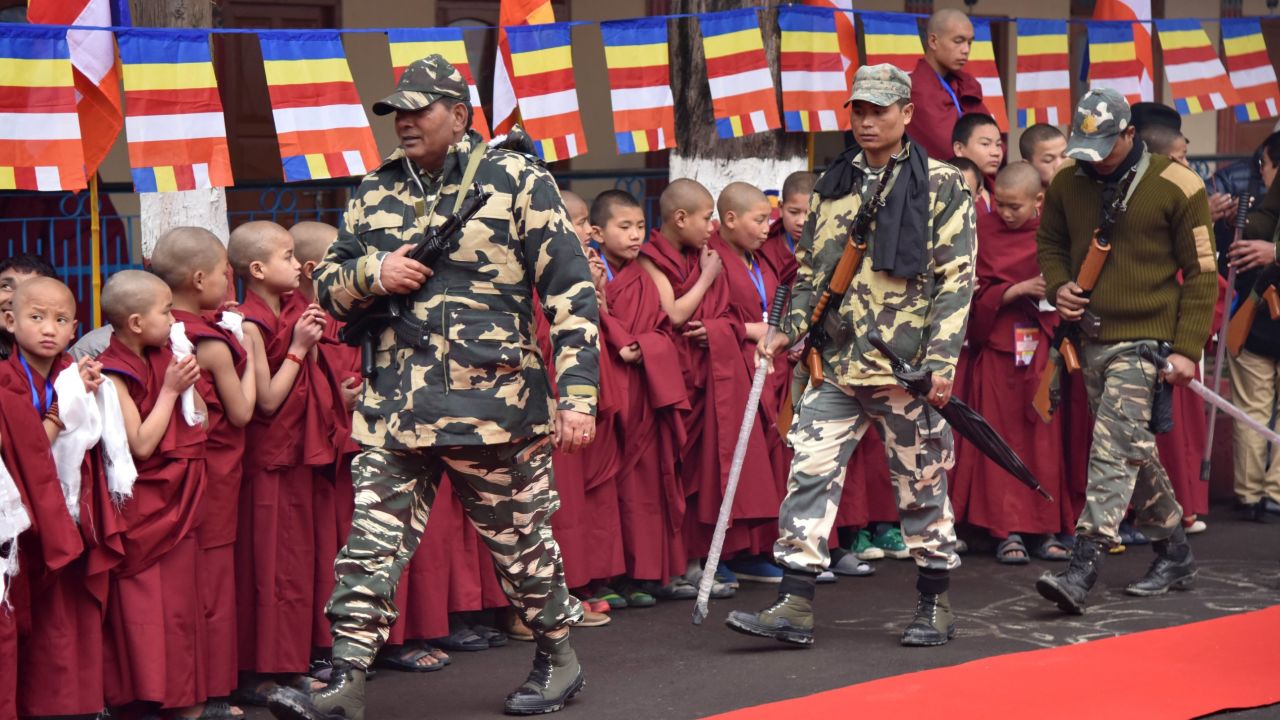 Indian security personnel walk past Buddhist monks as they wait for the Dalai Lama in Bomdila in India's northeastern state of Arunachal Pradesh on April 4, 2017.