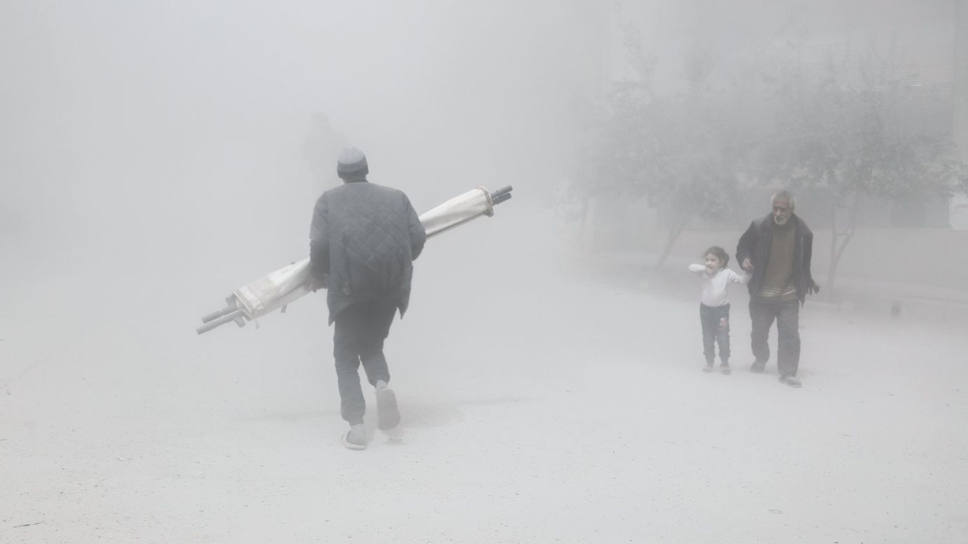 A man and girl walk past a man carrying a folded stretcher after a reported airstrike in Hamouria, Syria, on Tuesday, April 4.