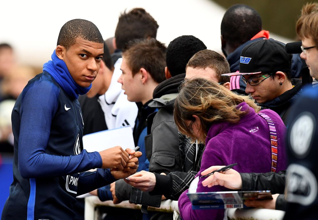 French national football team forward Kylian Mbappe (L) signs an autograph before a training session.