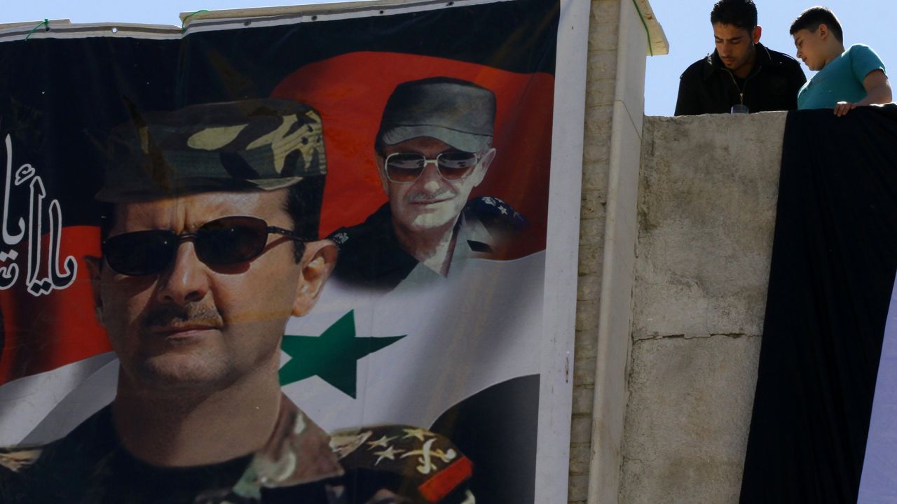 Syrians look down at a poster of Syrian President Bashar al-Assad (L) and his late father and predecessor Hafez al-Assad in Damascus, as they watch the tourist train pass following the re-opening ceremony of the rail route between two neighbourhoods in the Syrian capital, Raboeh and Dumar, on May 1, 2015. AFP PHOTO / LOUAI BESHARA        (Photo credit should read LOUAI BESHARA/AFP/Getty Images)