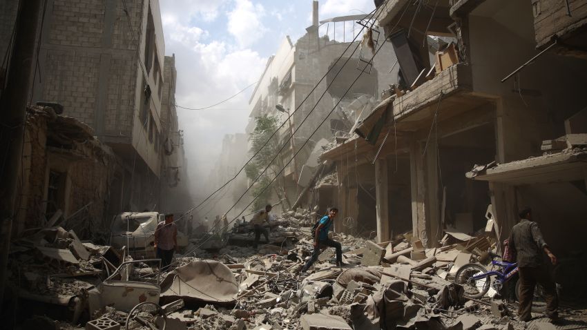 Syrians walk amid the rubble of destroyed buildings following reported air strikes by regime forces in the rebel-held area of Douma, east of the capital Damascus, on August 30, 2015. More than 240,000 people have been killed since Syria's conflict began in March 2011, and half of the country's population has been displaced by the war. AFP PHOTO / ABD DOUMANY / AFP / ABD DOUMANY        (Photo credit should read ABD DOUMANY/AFP/Getty Images)