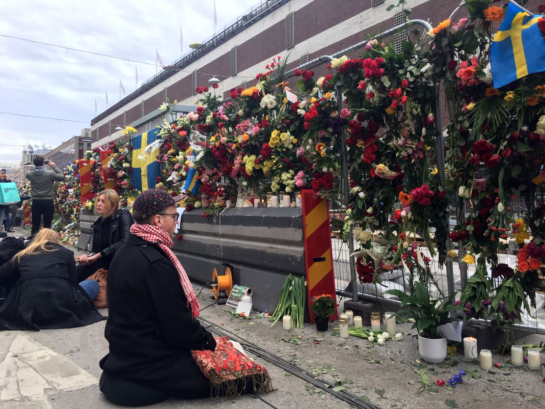 A mourner prays at the wall of flowers memorial that has sprung up down the street from the site of the Stockholm attack.