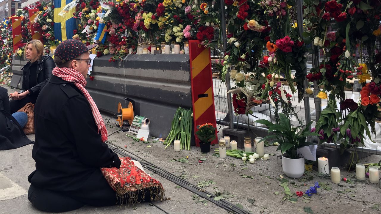 A mourner prays at the wall of flowers memorial that has sprung up down the street from the site of the Stockholm attack.