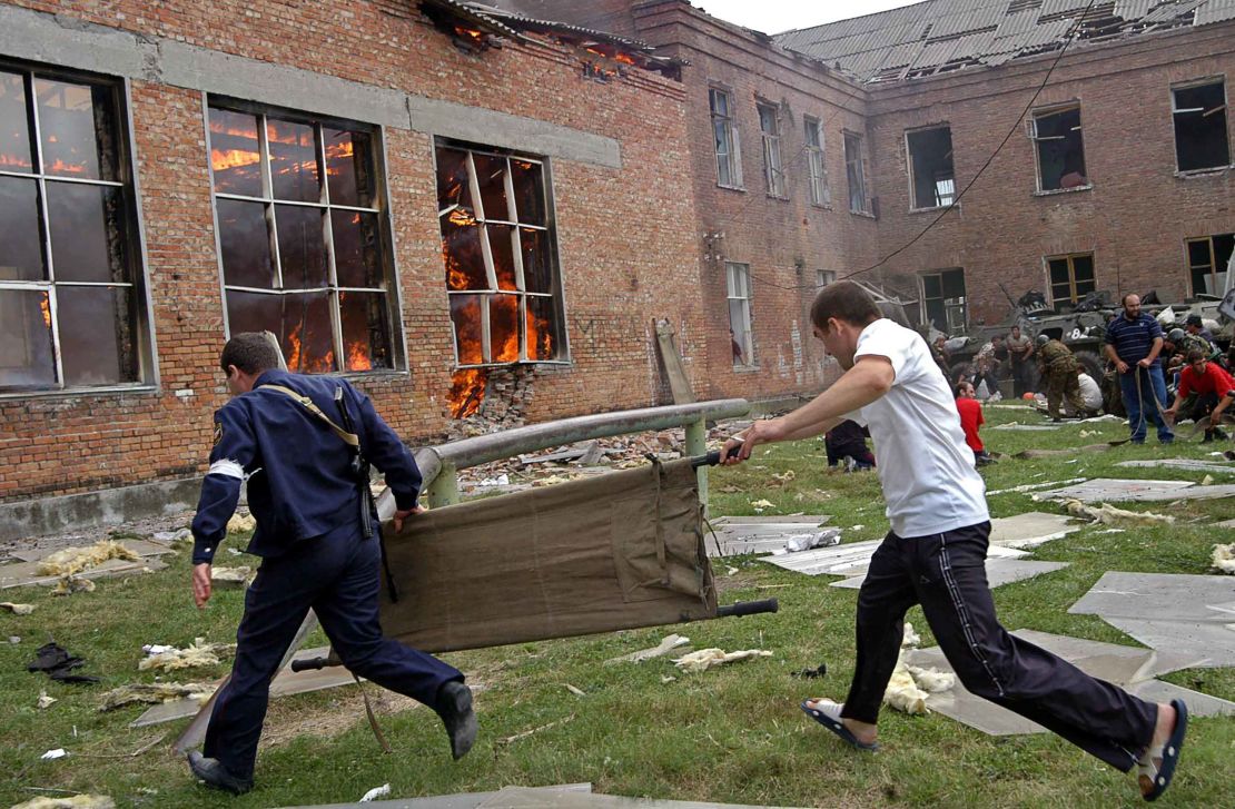 Two volunteers carry a stretcher as they approach a burning school during a rescue operation on September 3, 2004, in Beslan, Northern Ossetia.