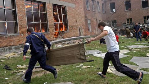 Two volunteers carry a stretcher as they approach a burning school during a rescue operation on September 3, 2004, in Beslan, Northern Ossetia.