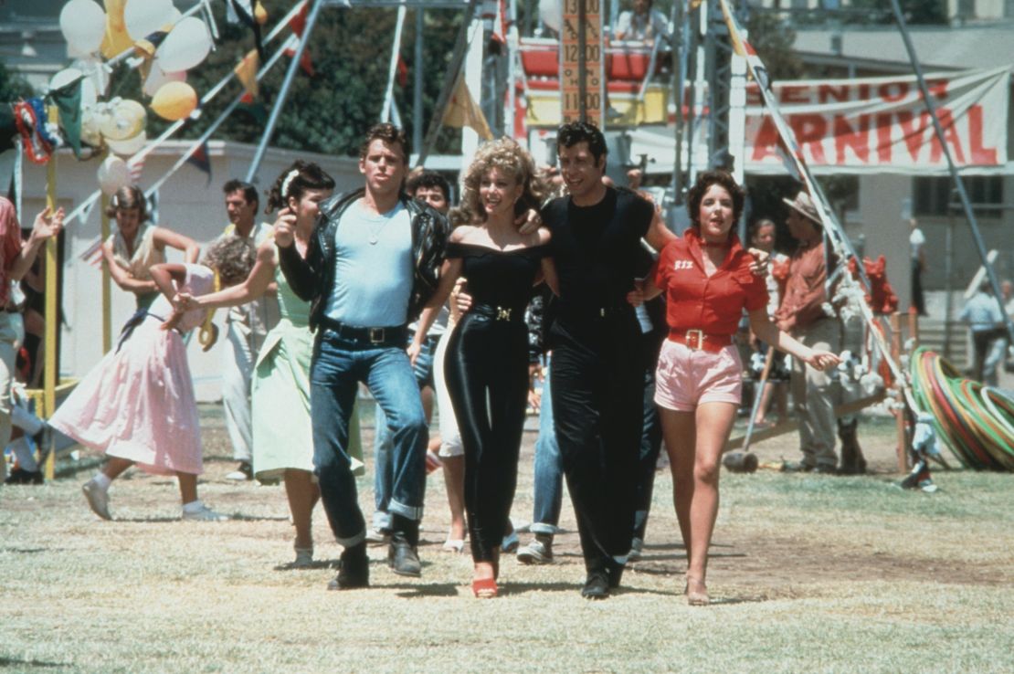 Jeff Conaway, Olivia Newton-John, John Travolta and Stockard Channing walk arm in arm at a carnival in a still from the film, 'Grease.' 