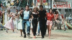 Jeff Conaway, Olivia Newton-John, John Travolta and Stockard Channing walk arm in arm at a carnival in a still from the film, 'Grease.'