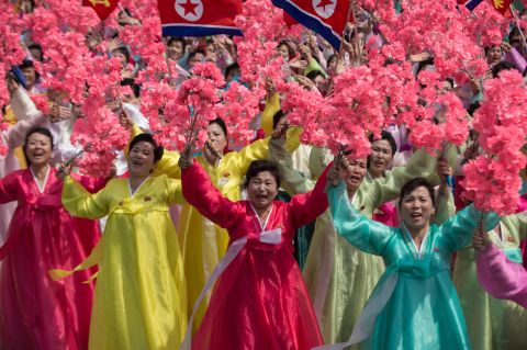 Women wearing traditional Korean dress wave flowers and shout slogans as they pass North Korea's leader Kim Jong-Un.