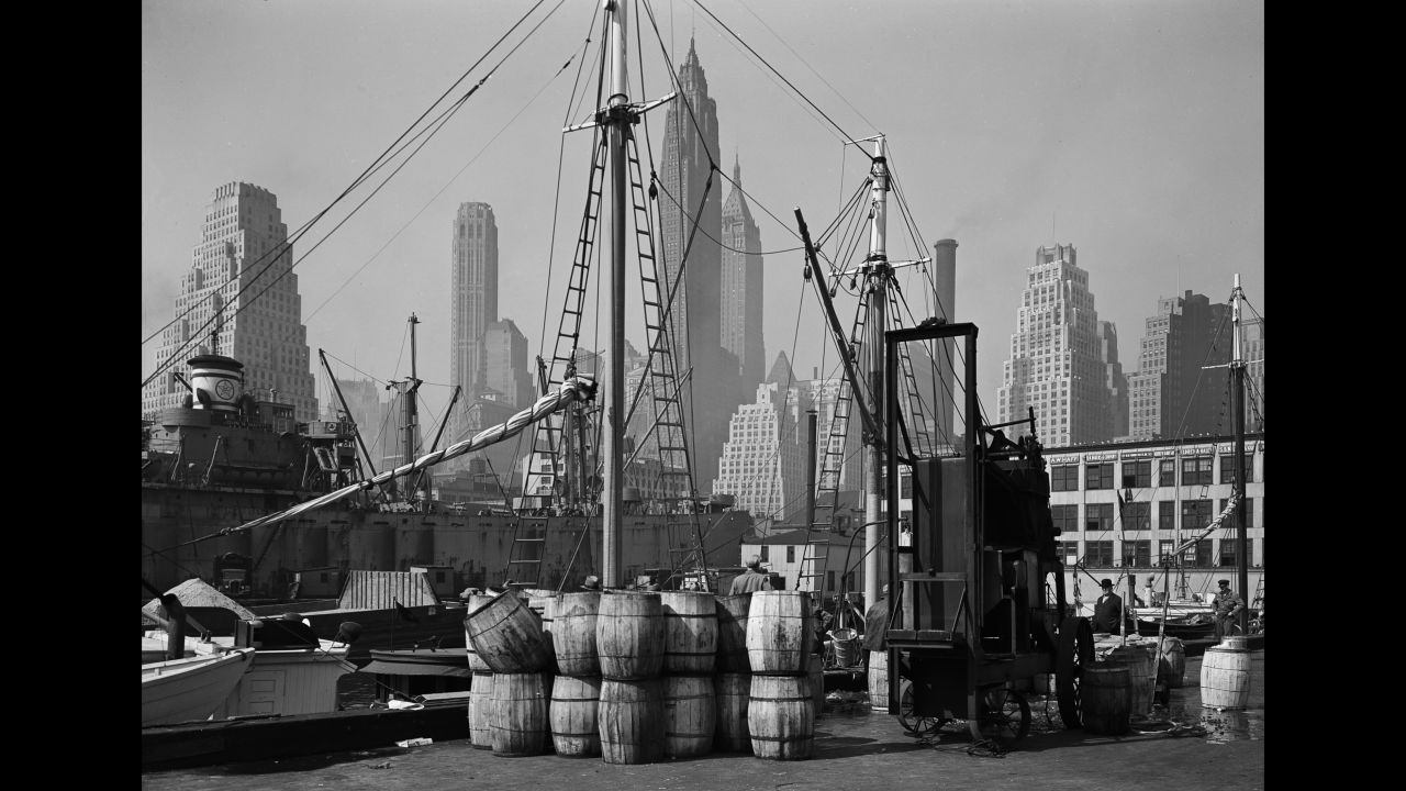 A view of the Fulton Fish Market in 1946. A ship sits in the foreground, while skyscrapers stand tall in the background.