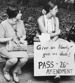 Young woman holding a sign that reads, 'Give us liberty or give us death! Pass the 26th Amendment!' while sitting next to a middle-aged woman on a bench at an Equal Rights demonstration, 1970s. (Photo by Hulton Archive/Getty Images)
