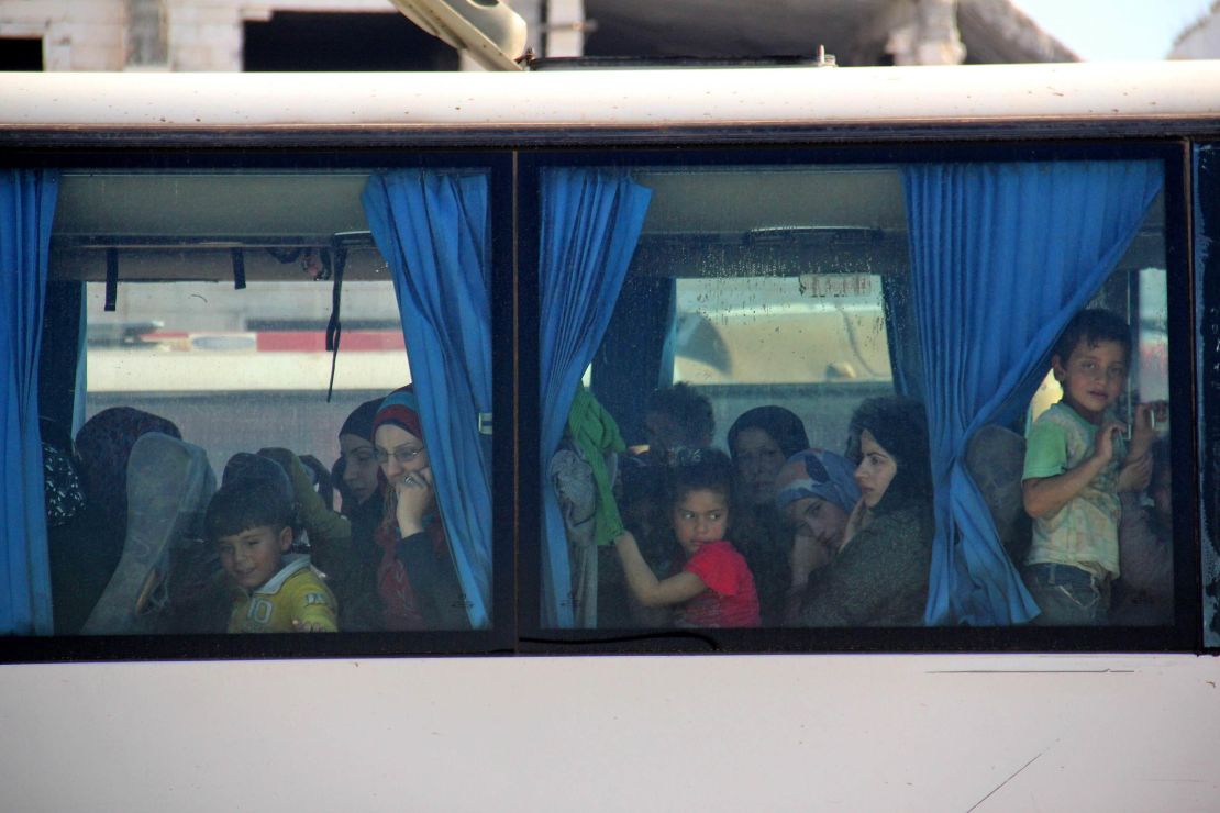 Women and children look out from a bus window.