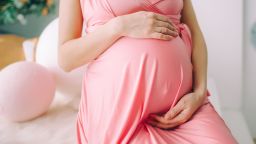 Charming tummy (belly) which the pregnant woman in a coral dress embraces