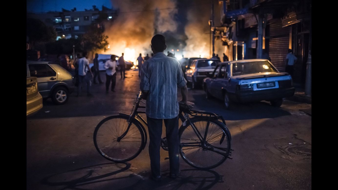 A cyclist watches a fire caused by the explosion of a mortar shell during fighting between government and opposition forces near the Old City of Damascus. (August 24, 2013)