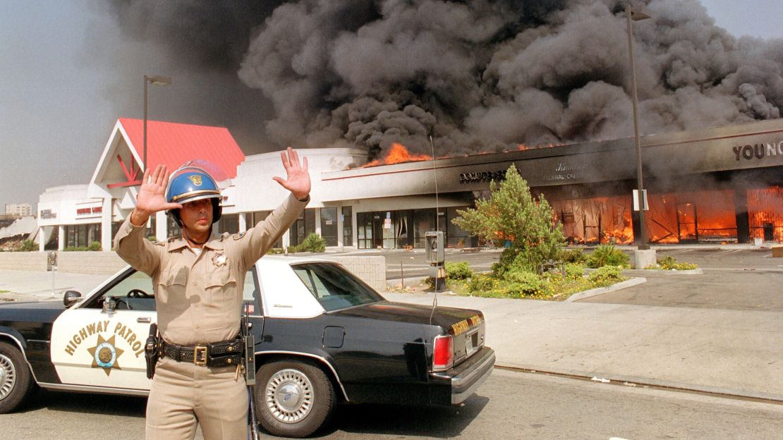 A California Highway patrolman directs raffic around a shopping center engulfed in flames in Los Angeles, 30 April 1992.
