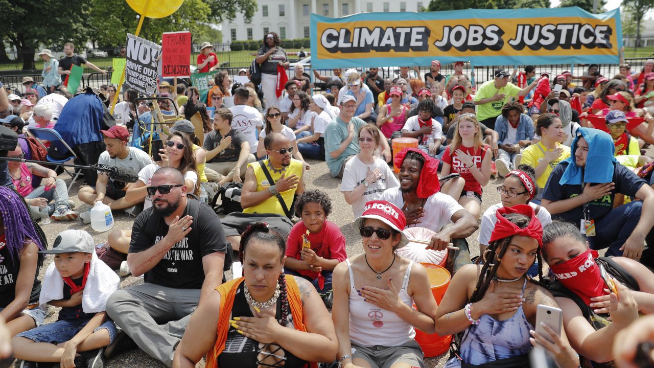 Demonstrators sit on the ground in front of the White House.