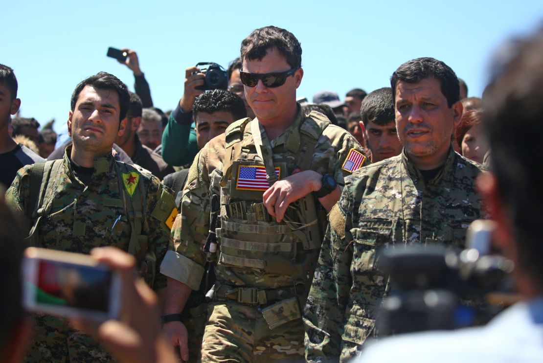 An officer, from the US-led coalition stands alongside Kurdish fighters from the People's Protection Units (YPG) at the site of Turkish airstrikes on YPG positions in Syria.