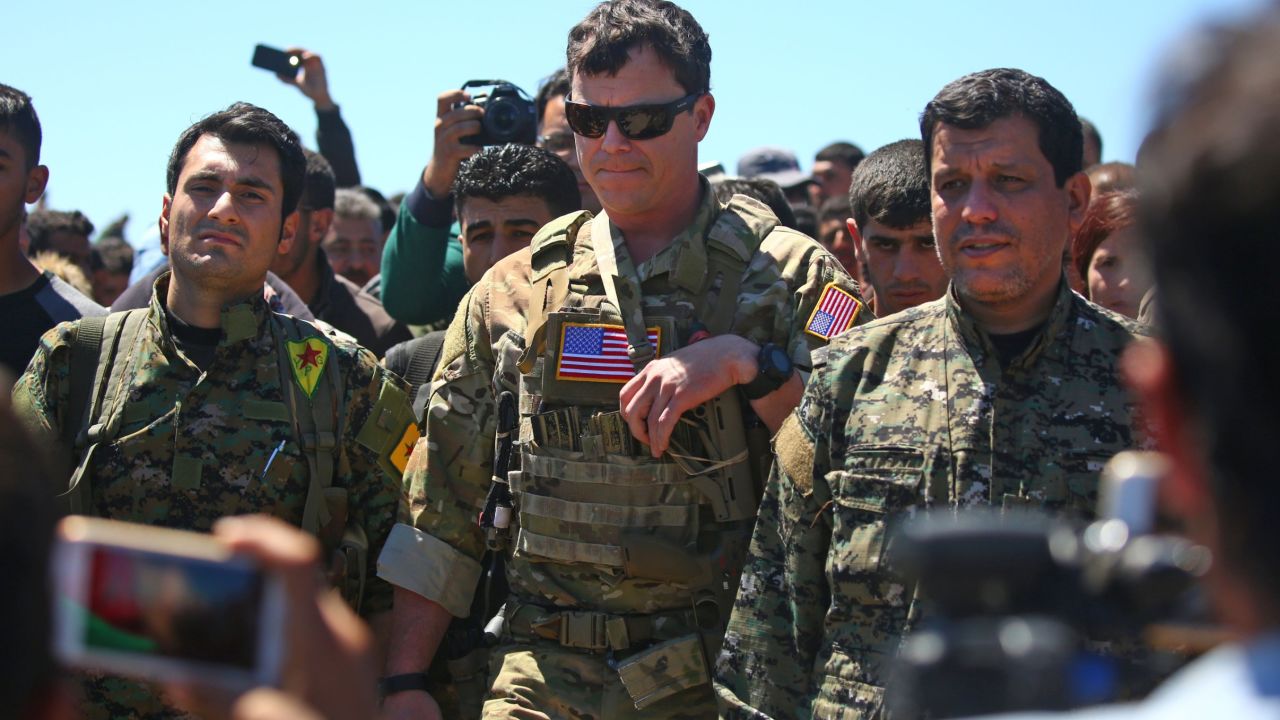 An officer from the US-led coalition stands alongside Kurdish fighters from the People's Protection Units (YPG).