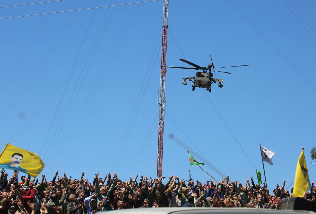 Kurds wave flags as a medical helicopter, from the US-led coalition, flies over the site of Turkish airstrikes near northeastern Syrian Kurdish town of Derik, known as al-Malikiyah in Arabic, on April 25, 2017.
