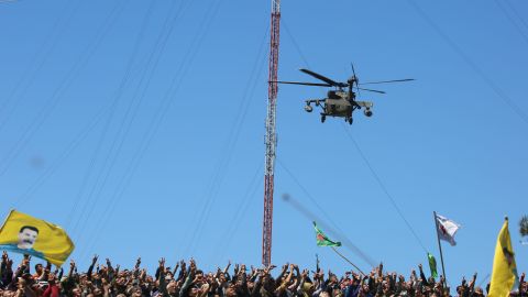 Kurds wave flags and cheer as a medical helicopter from the US-led coalition on Wednesday flies over the Turkish airstrikes site near Derik, Syria.