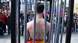 An activist stands naked, wrapped in a rainbow flag, in a mock cage in front of the Chancellery in Berlin on April 30, 2017, during a demonstration calling on Russian President to put an end to the persecution of gay men in Chechnya. The protestors called on German Chancellor Angela Merkel, who will meet Putin in Sochi on May 2, 2017, to raise the issue with him. / AFP PHOTO / John MACDOUGALL        (Photo credit should read JOHN MACDOUGALL/AFP/Getty Images)