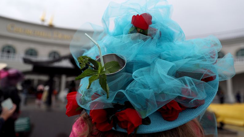 A woman uses her festive hat as a cup holder before the race. The <a href="index.php?page=&url=https%3A%2F%2Fwww.kentuckyderby.com%2Fhistory%2Ftraditions%2Fmint-julep" target="_blank" target="_blank">mint julep</a> is the traditional beverage of Churchill Downs and the Kentucky Derby.