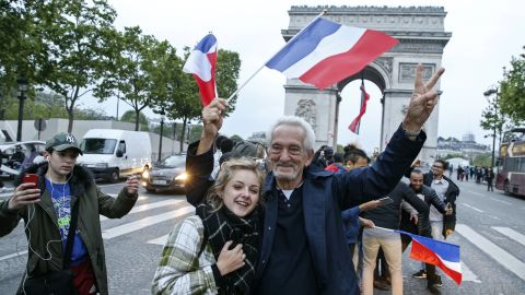 A man, flanked by a young woman, waves a French national flag next to people gesturing and shouting on the French avenue of the Champs Elysees.