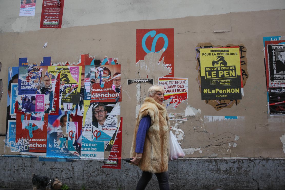 A woman walks past election campaign posters in Paris' 18th district. One poster, in yellow, encourages voters to vote against Marine Le Pen. 