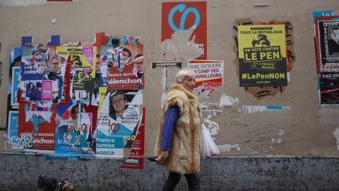 A woman walks past election campaign posters in Paris' 18th district. One poster, in yellow, encourages voters to vote against Marine Le Pen.