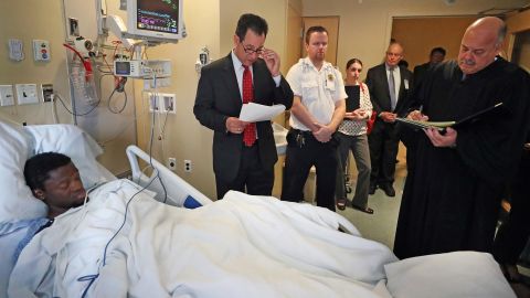 Bampumim Teixeira is arraigned from his hospital bed at Tufts Medical Center in Boston on Monday.