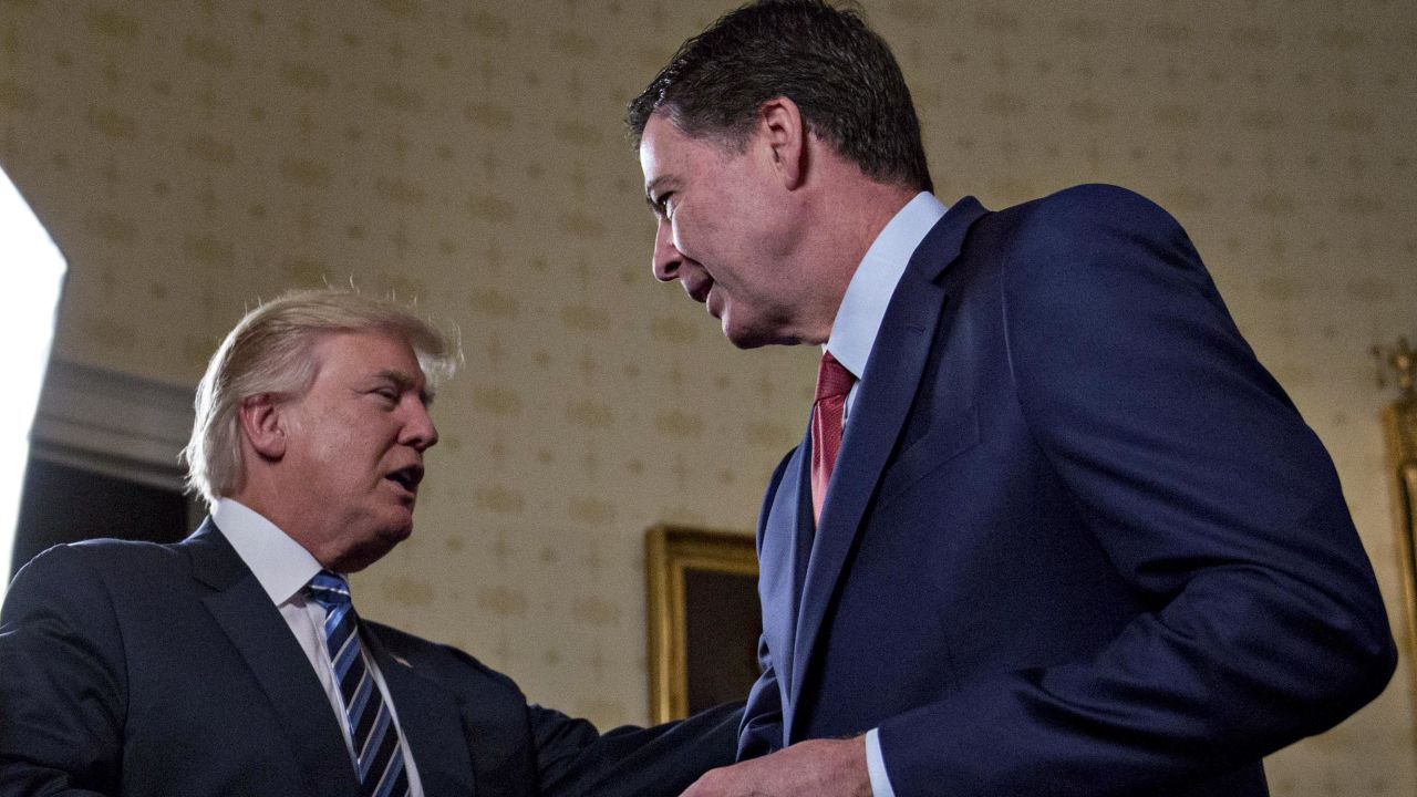 WASHINGTON, DC - JANUARY 22: U.S. President Donald Trump (C) shakes hands with James Comey, director of the Federal Bureau of Investigation (FBI), during an Inaugural Law Enforcement Officers and First Responders Reception in the Blue Room of the White House on January 22, 2017 in Washington, DC. Trump today mocked protesters who gathered for large demonstrations across the U.S. and the world on Saturday to signal discontent with his leadership, but later offered a more conciliatory tone, saying he recognized such marches as a "hallmark of our democracy." (Photo by Andrew Harrer-Pool/Getty Images)