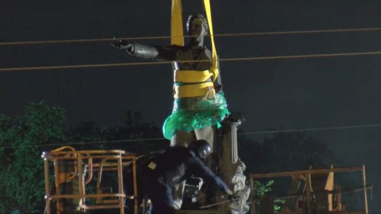 A worker chisels away at the statue's feet to release it from the base.