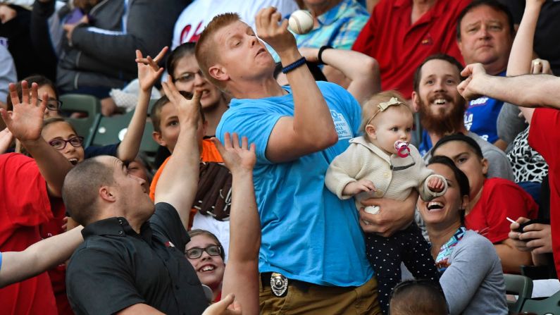 Mark Ehlke holds his 1-year-old daughter, Elsie, while catching a foul ball during a minor-league game in Peoria, Illinois, on Friday, May 12.