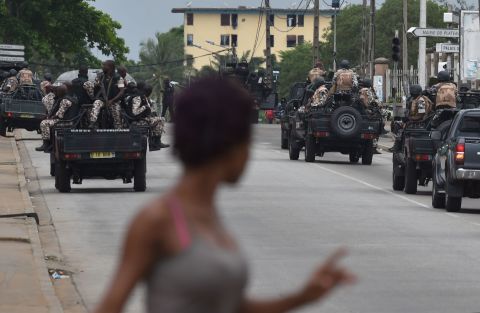 A woman walks past Ivorian soldiers patrolling by Ivory Coast's army headquarters, the Gallieni military camp, in Abidjan.<br />Banks, school and international institutions have closed during the uprising, leaving usually busy streets deserted. 