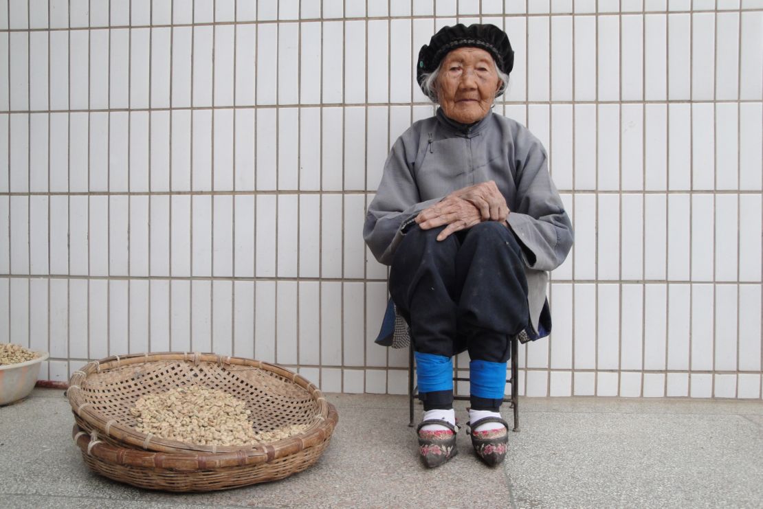 An elderly woman with bound feet sits by a basket in Yunnan, China