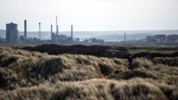 A man explores the sand dunes adjacent to the beach, with heavy industry located in the town of Redcar on the horizon, near Hartlepool, northern England on March 8, 2017. 