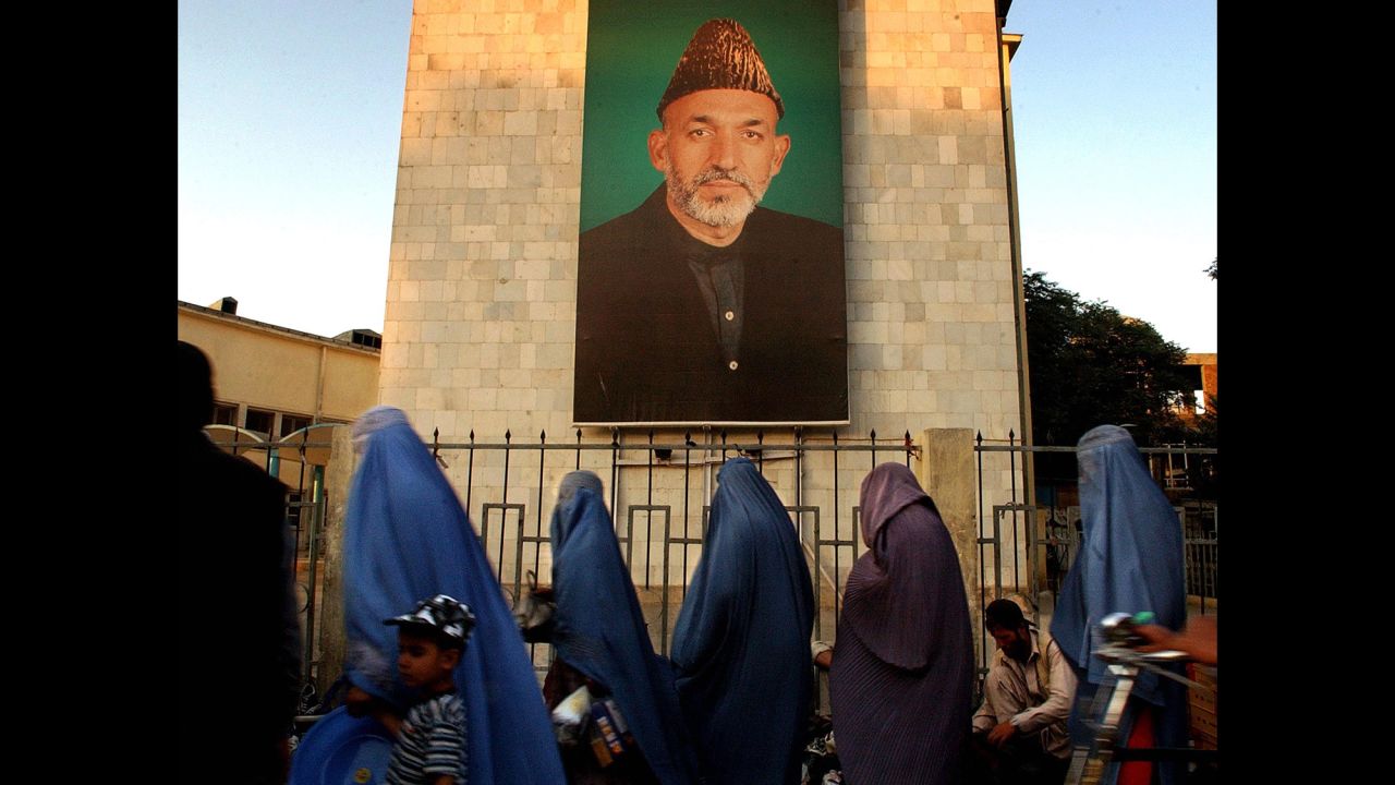 Afghan women walk past a portrait of Karzai in Kabul on October 26, 2004. Karzai had been in a leadership role since December 2001, when an interim government was formed after the Taliban lost its last major stronghold.