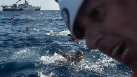 Refugees and migrants swim towards a rescue craft as a rescue crewmember from the Migrant Offshore Aid Station (MOAS) 'Phoenix' vessel pulls a man on board.